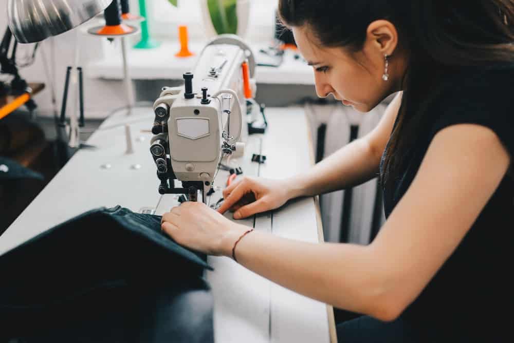 female artisan threading black leather sewing machine