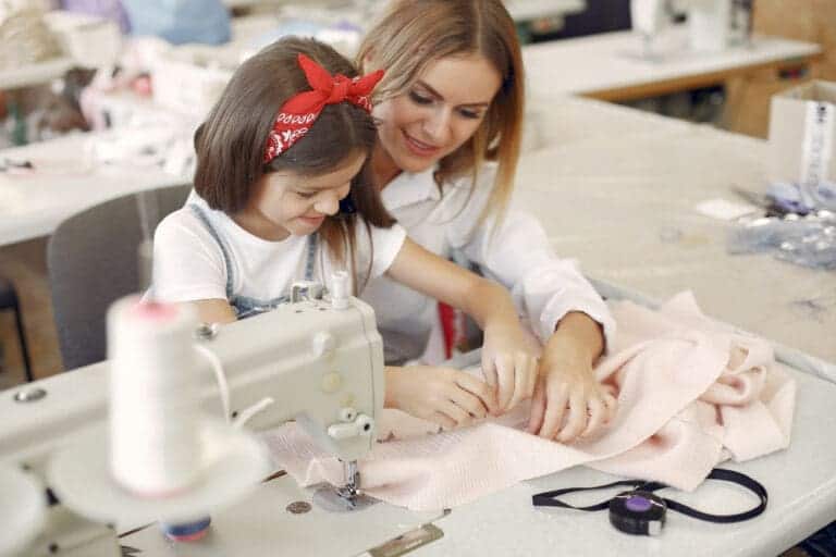 mother with little daughter sew clothes factory