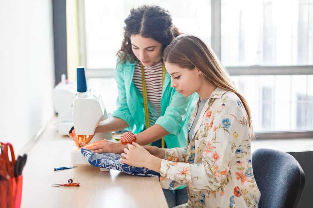 Are You A Student Wants To Teach A Friend How To Sew? Here's What You Do! 1 pretty seamstress teaching girl working with sewing machine sewing classes with window background modern sewing workshop