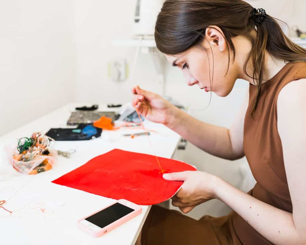 young woman sewing red cloth with needle